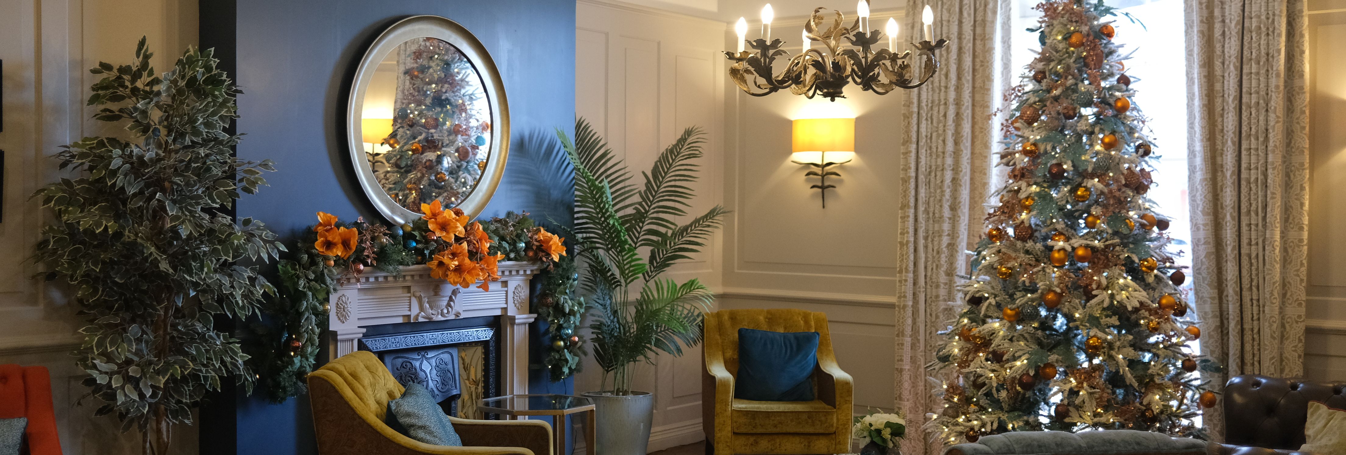 Elegant lounge decorated for Christmas with a festive tree, armchairs, fireplace, and cozy lighting.