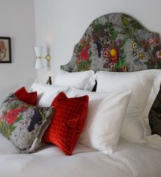 A neatly made bed with a floral-patterned headboard and decorative pillows in red and floral designs.