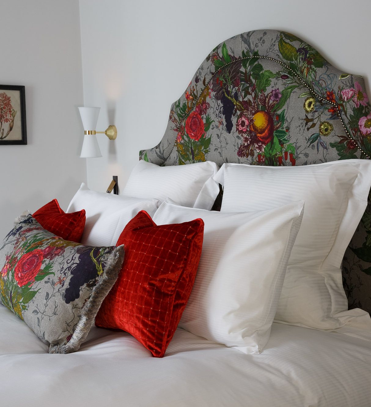 A neatly made bed with a floral-patterned headboard and decorative pillows in red and floral designs.