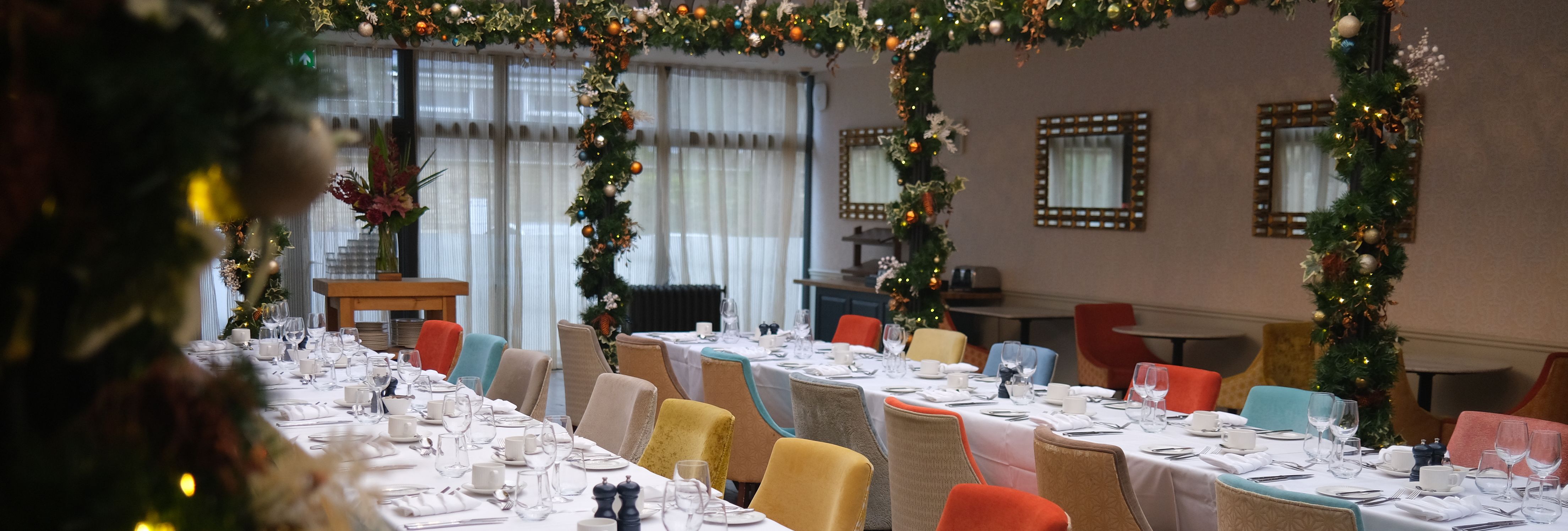 Elegant dining area with long tables set for a meal, surrounded by colorful chairs and festive holiday decorations.