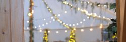 Decorated event tent with string lights, wooden furniture, and greenery.