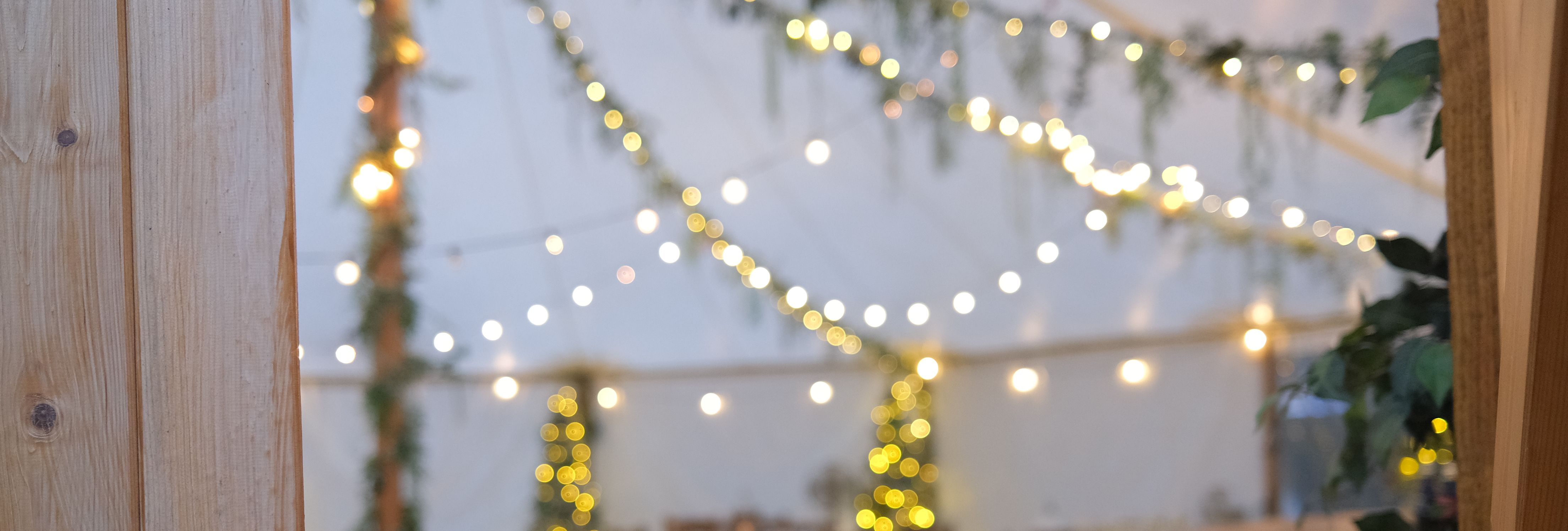 Decorated event tent with string lights, wooden furniture, and greenery.
