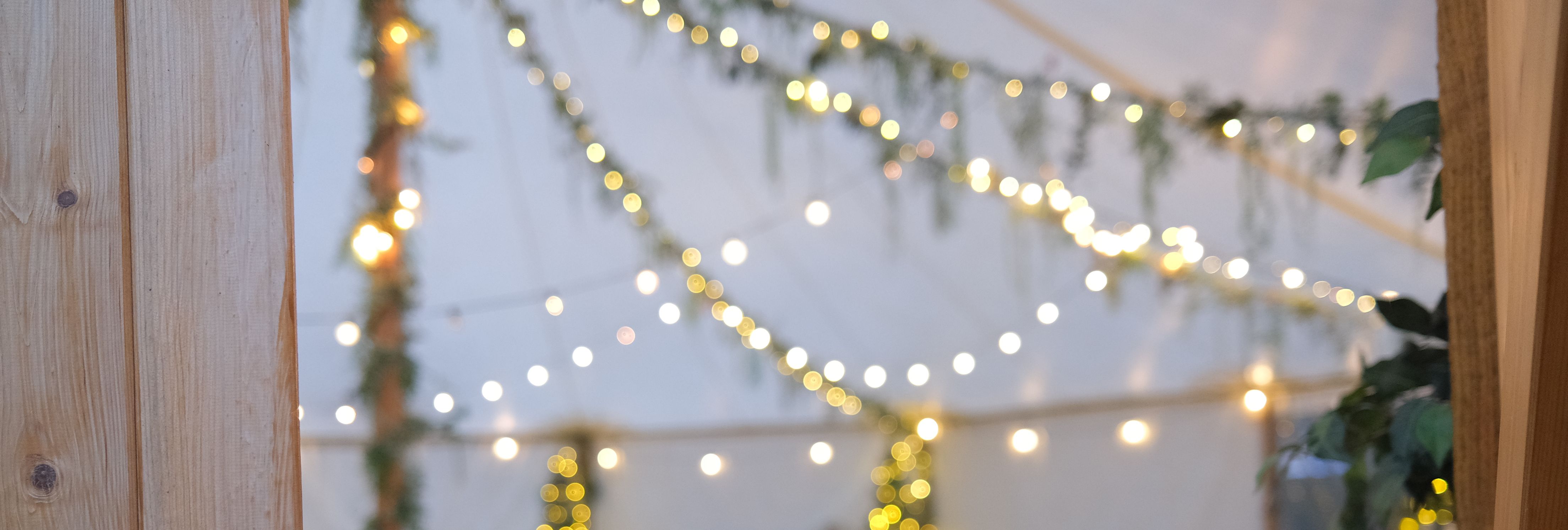 Decorated event tent with string lights, wooden furniture, and greenery.
