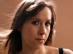 Woman with light brown hair wearing a black dress looking at the camera with a neutral expression