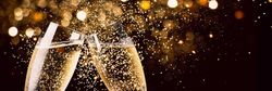 Two champagne glasses clinking with golden sparkling lights in the background