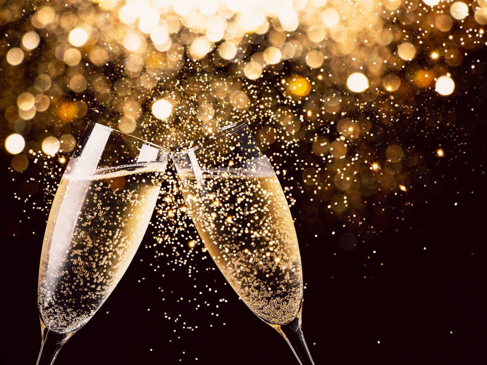 Two champagne glasses clinking with golden sparkling lights in the background