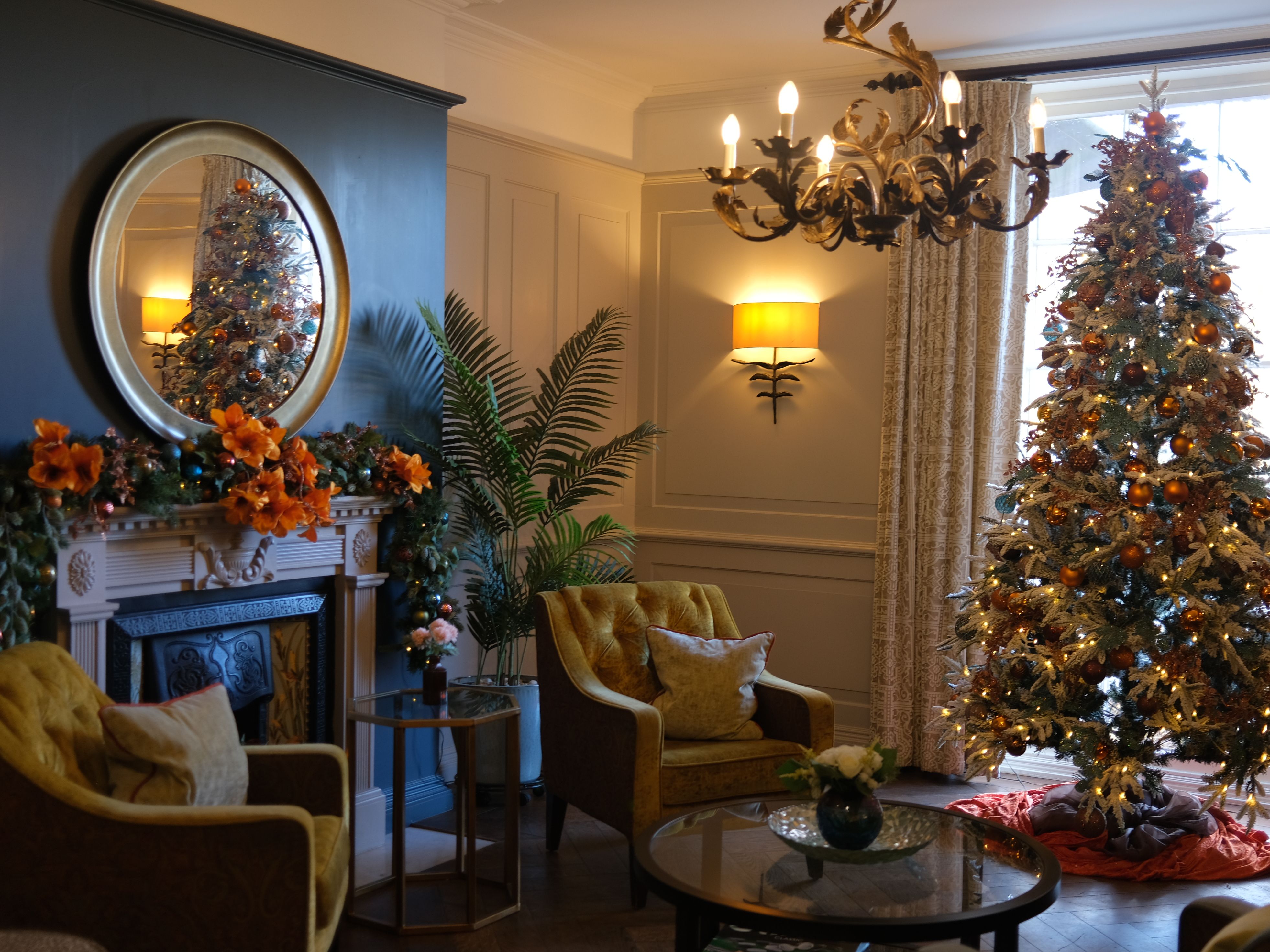 Elegant living room decorated for Christmas with a lit Christmas tree, fireplace garland, and cozy furniture