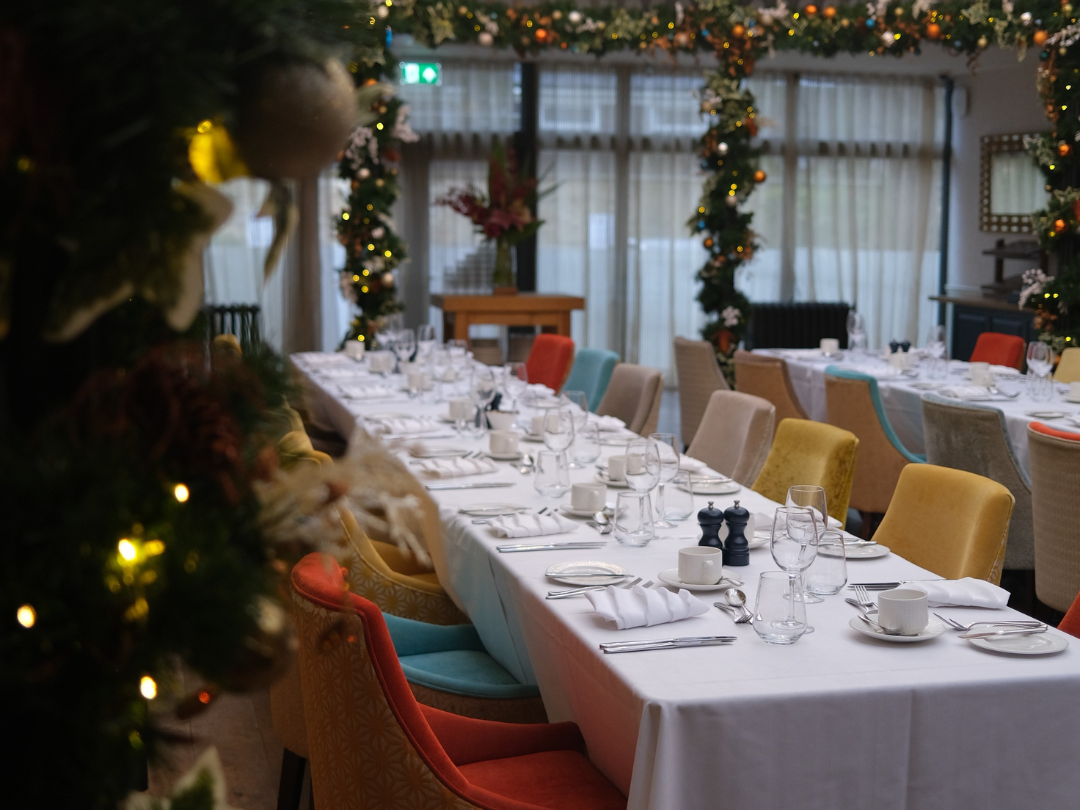 Long dining table set for a festive meal with colorful chairs and Christmas decorations.