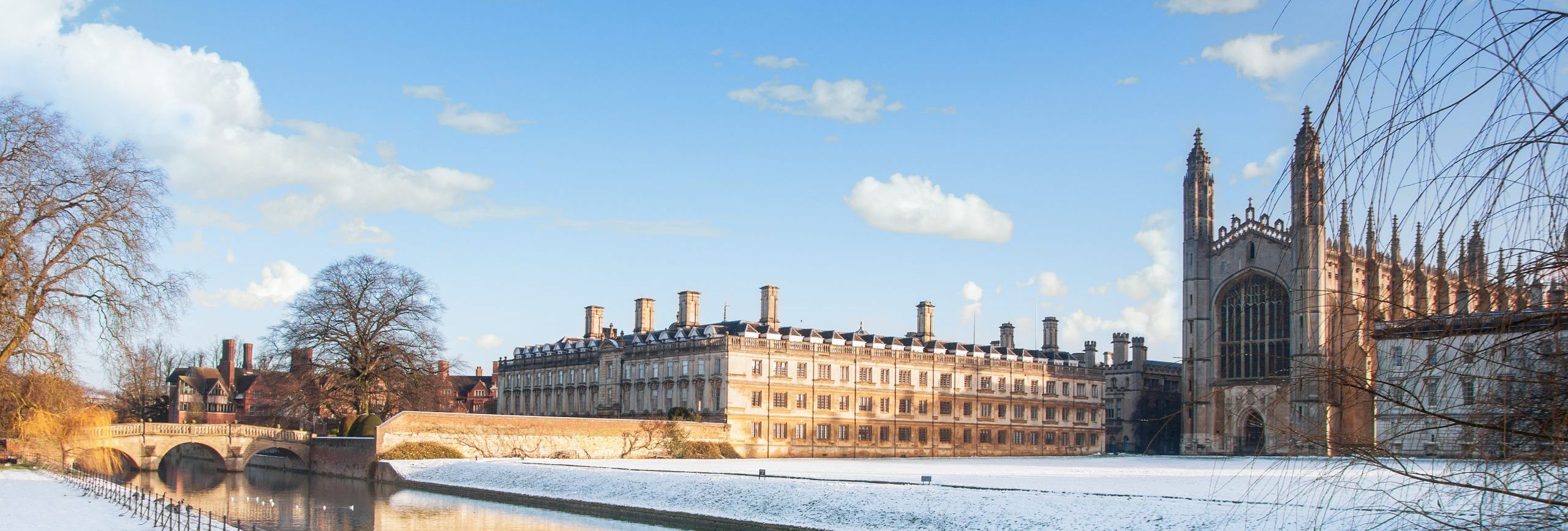 Kings College building and chapel in Cambridge, England, covered in snow during winter with the River Cam in the foreground.
