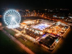 A brightly lit carnival at night with a large Ferris wheel, ice skating rink, and festive market booths