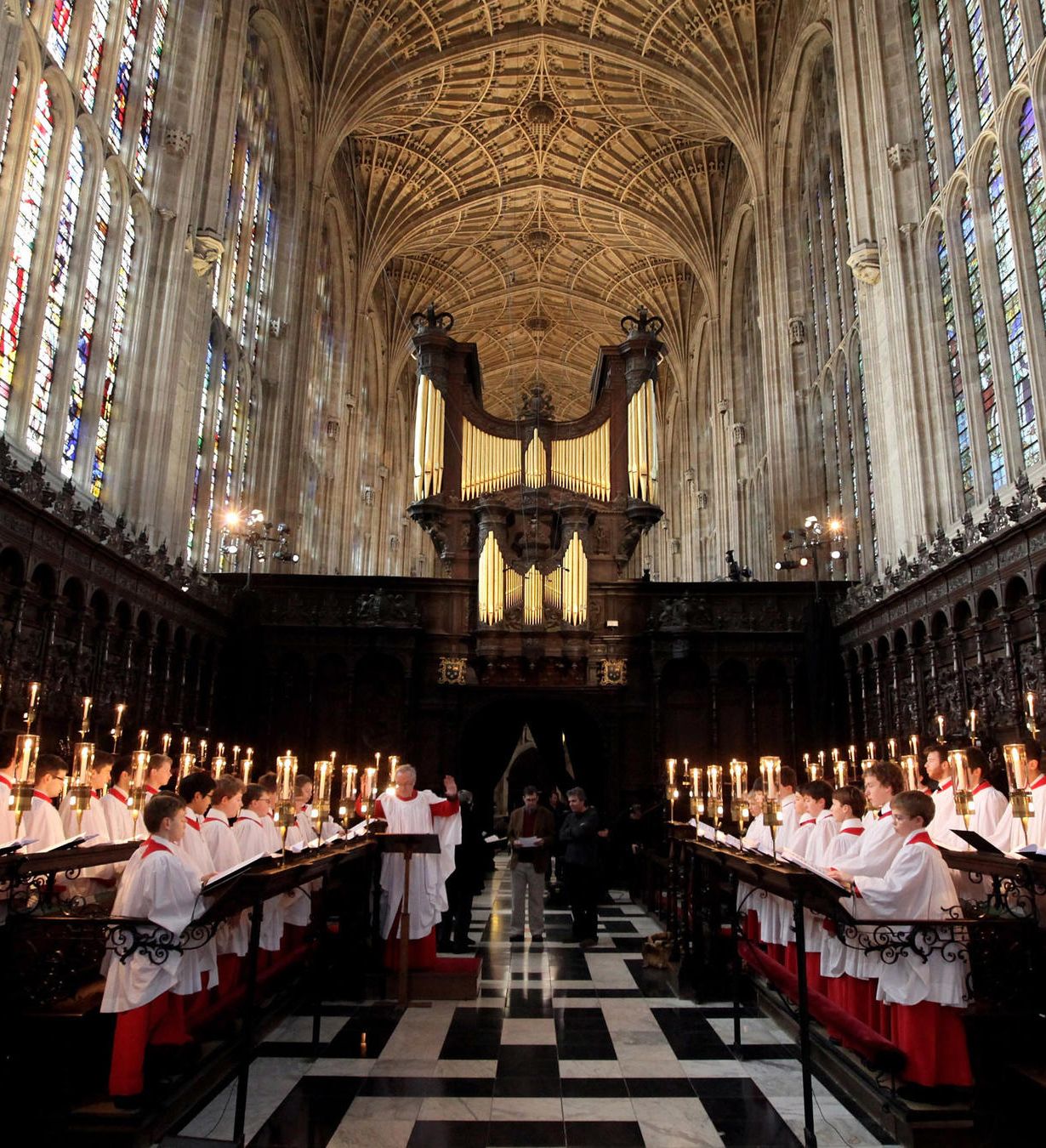 Choir singing in a grand cathedral with stained glass windows and ornate wooden stalls