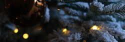 Close-up of a glittery bronze Christmas ornament hanging on a snow-frosted tree with warm lights.