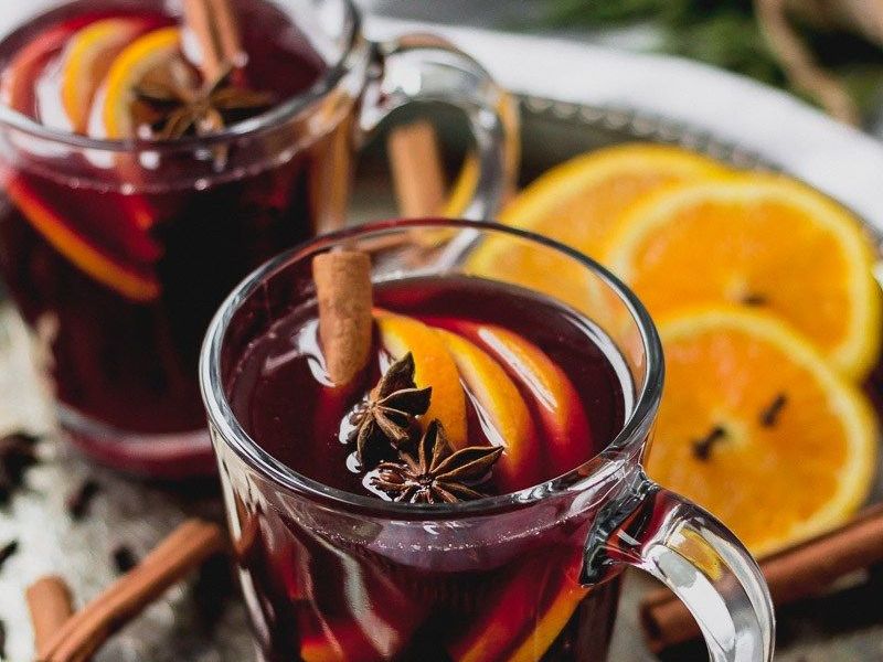 Two clear mugs of mulled wine garnished with orange slices, cinnamon sticks, and star anise on a silver tray.