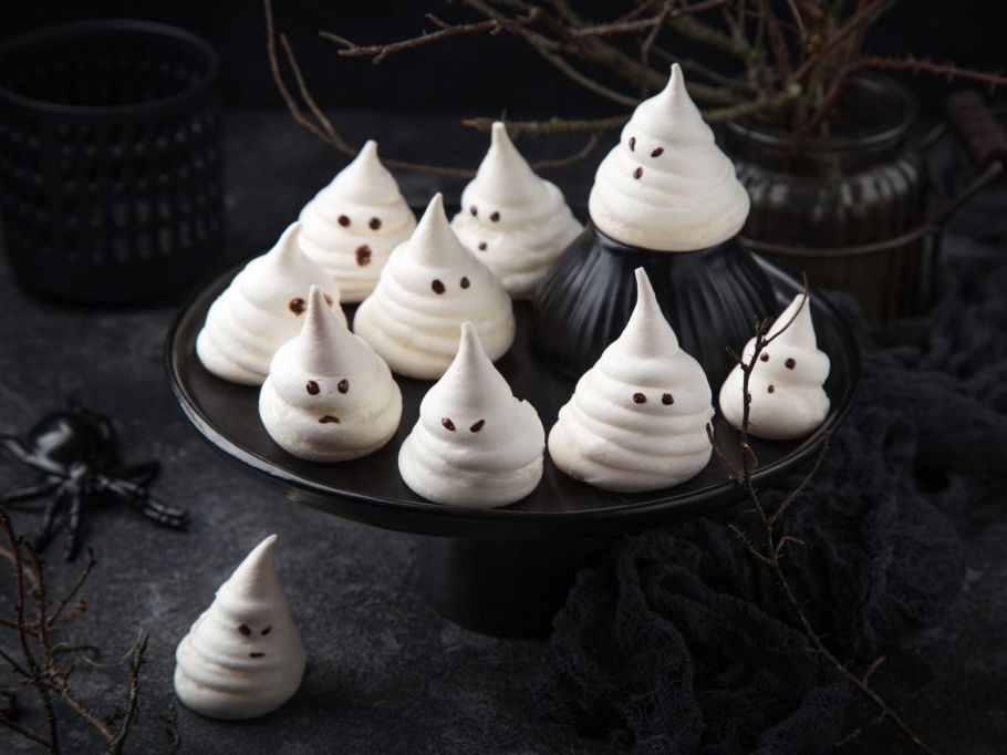 Meringue ghost cookies displayed on a black cake stand, surrounded by spooky Halloween decorations.