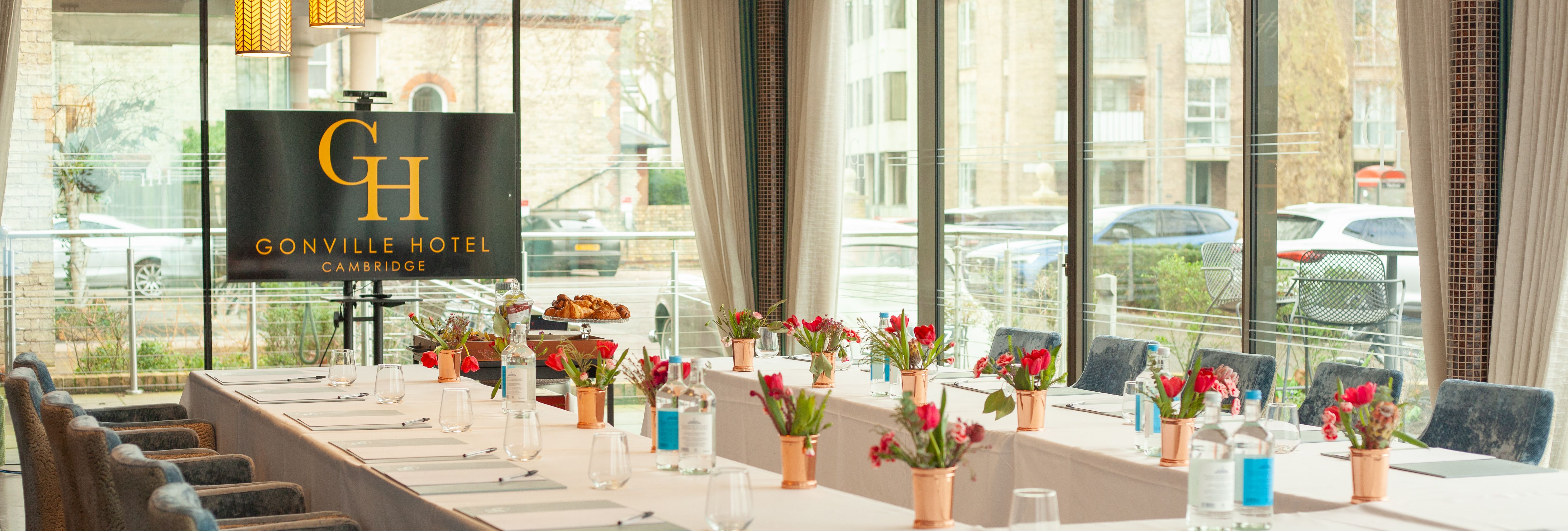 Elegant meeting room at Gonville Hotel Cambridge with U-shaped table setup, floral centerpieces, and large windows.
