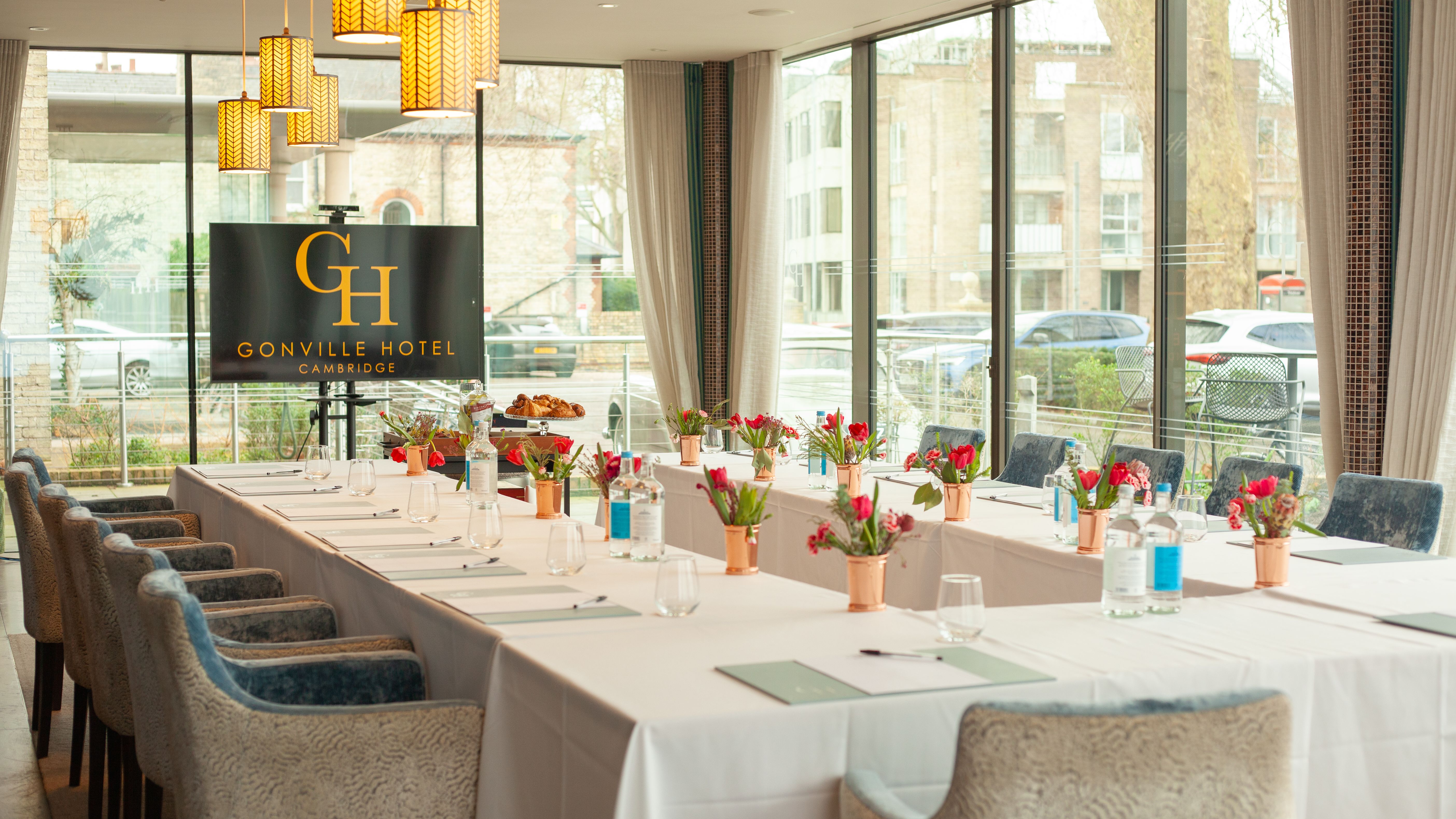 Elegant meeting room at Gonville Hotel Cambridge with U-shaped table setup, floral centerpieces, and large windows.