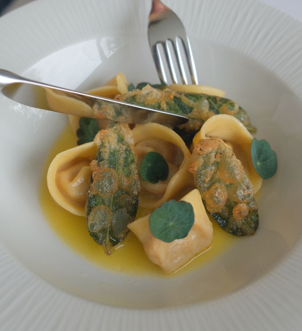 Gourmet pasta dish with stuffed pasta, crispy sage leaves, and green herbs in a yellow sauce