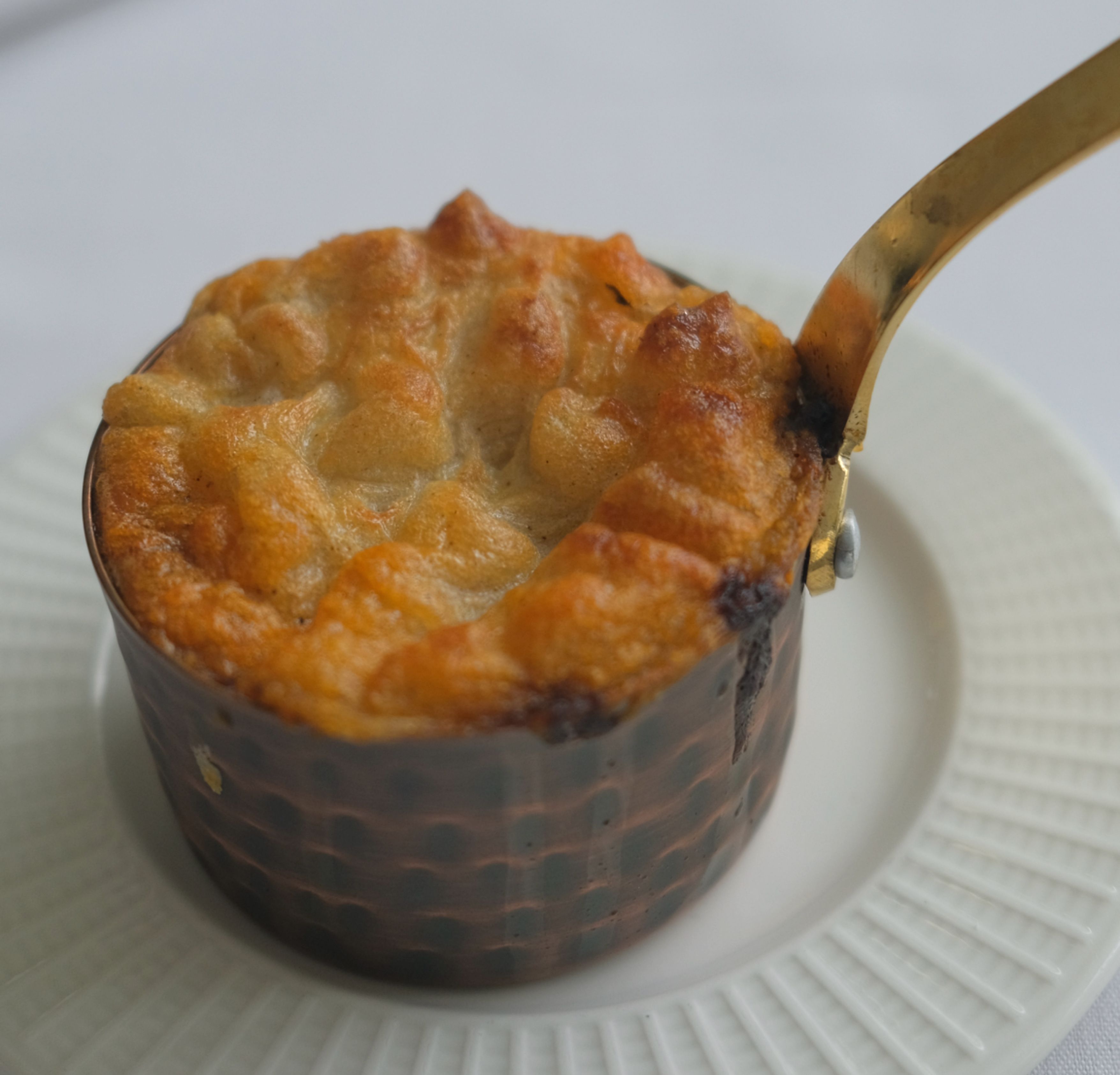 A golden-brown individual pot pie in a small pan on a white plate