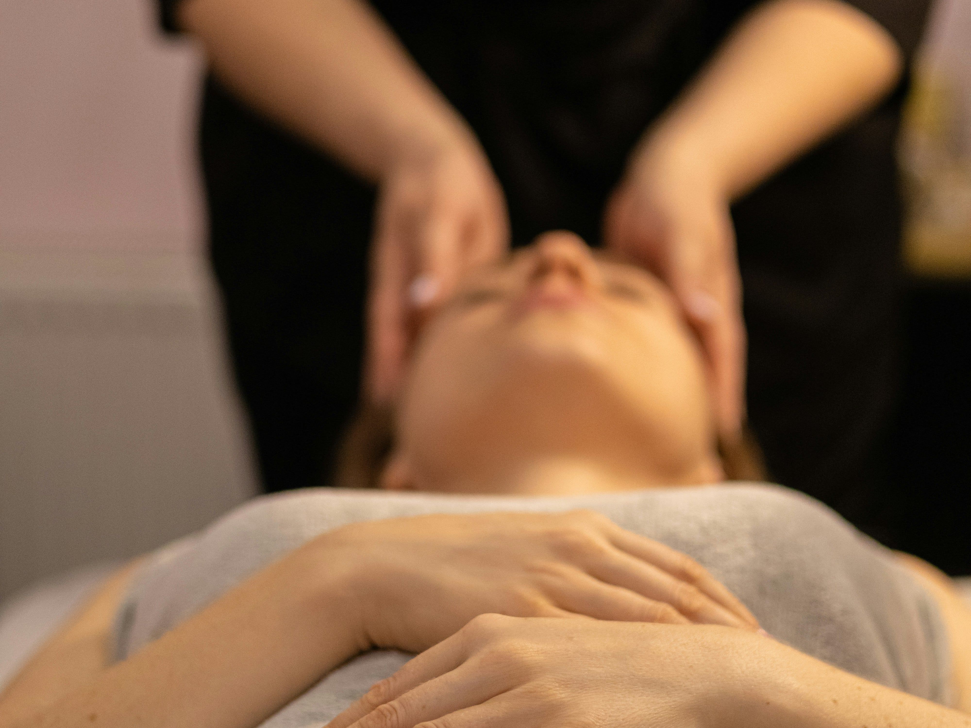 Person receiving a relaxing head massage at a spa, hands folded on chest, covered with a towel