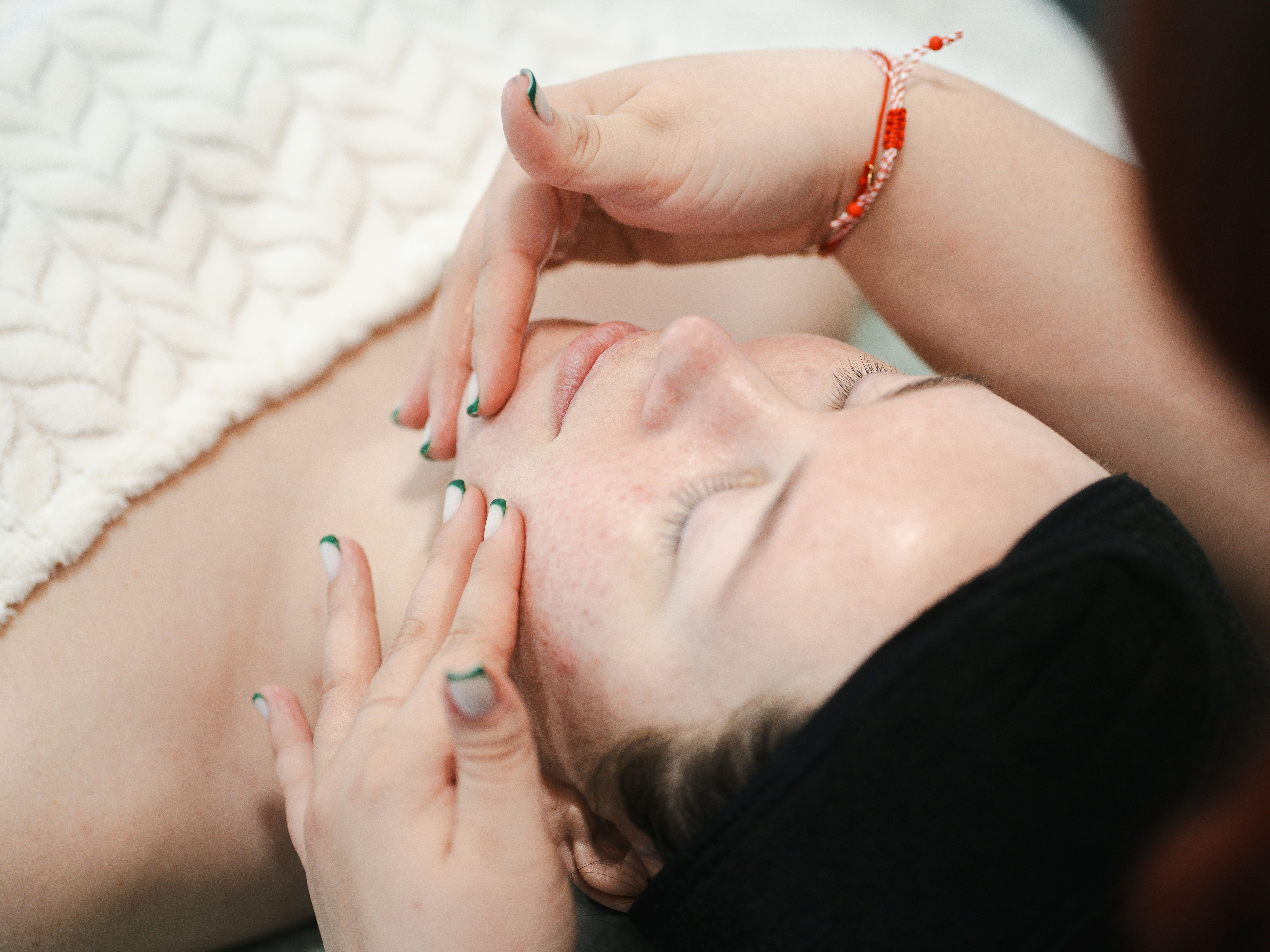 Person receiving a relaxing facial massage at a spa, lying under a textured white blanket with eyes closed