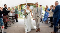 Bride and groom walking down the aisle at a wedding ceremony, smiling and holding hands, with guests applauding.