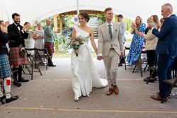 Bride and groom walking down the aisle at a wedding ceremony, smiling and holding hands, with guests applauding.