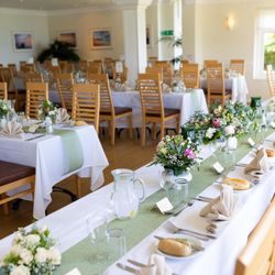 Elegant banquet hall set up for a formal event with decorated tables, wooden chairs, floral centerpieces, and place settings.