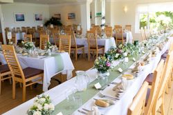 Elegant banquet hall set up for a formal event with decorated tables, wooden chairs, floral centerpieces, and place settings.