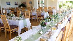 Elegant banquet hall set up for a formal event with decorated tables, wooden chairs, floral centerpieces, and place settings.