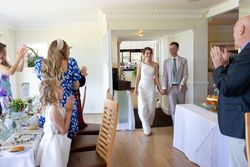 Bride and groom enter a wedding reception holding hands while guests applaud.