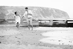 Couple walking barefoot on the beach, holding hands and laughing.