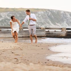 Bride and groom holding hands and running barefoot on a beach