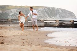 Bride and groom holding hands and running barefoot on a beach