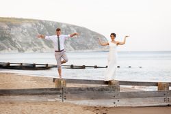 Bride and groom balancing playfully on wooden beams at a beach