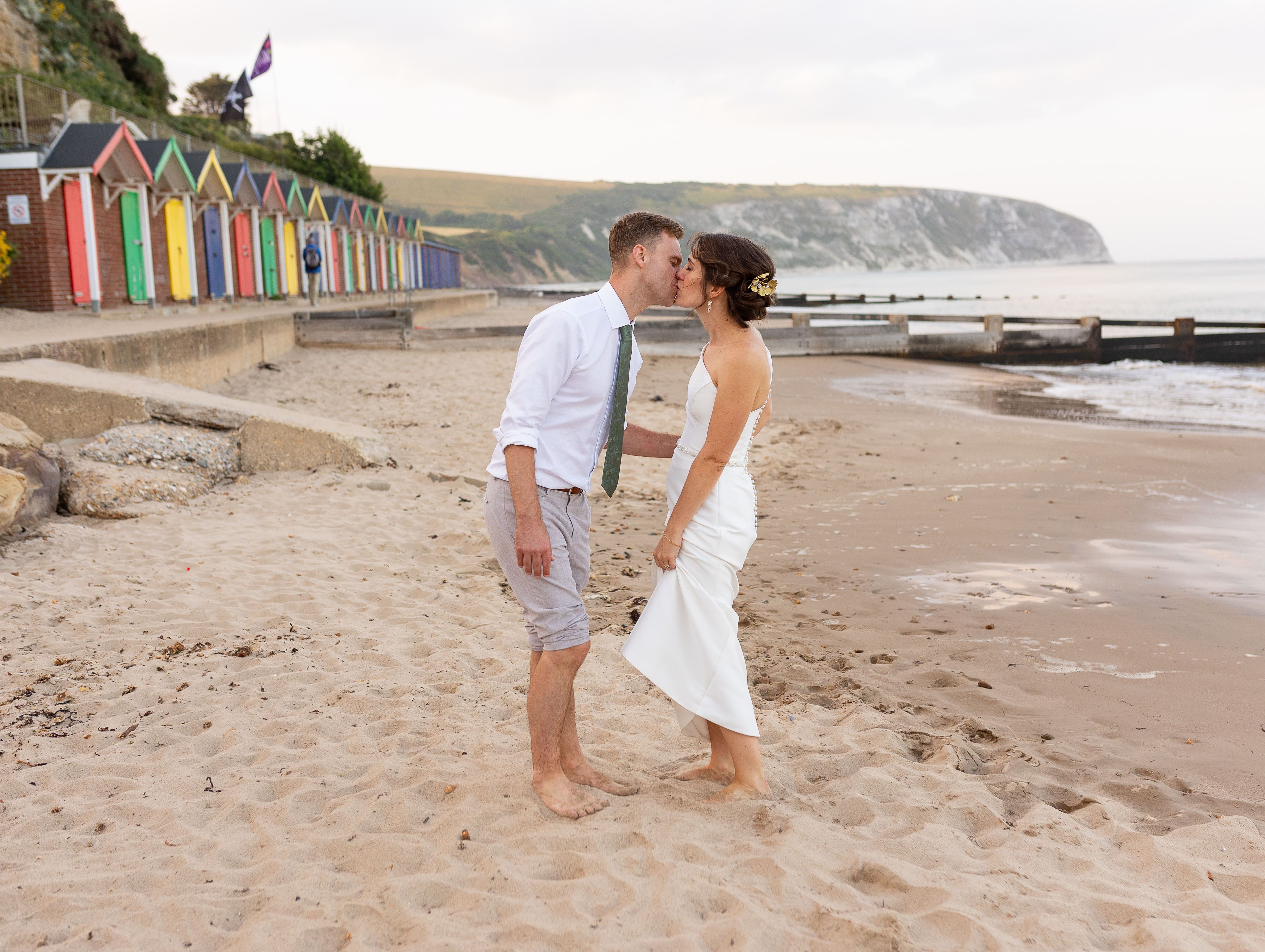 Couple kissing on a sandy beach with colorful beach huts in the background