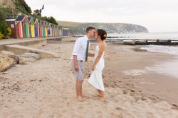 Couple kissing on a sandy beach with colorful beach huts in the background