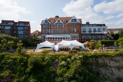Large brick hotel with white marquee tent on the lawn overlooking a cliff
