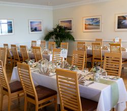 Elegant dining room with wooden chairs and decorated tables set for a formal event.