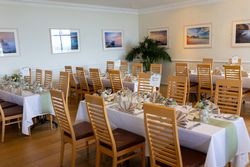 Elegant dining room with wooden chairs and decorated tables set for a formal event.