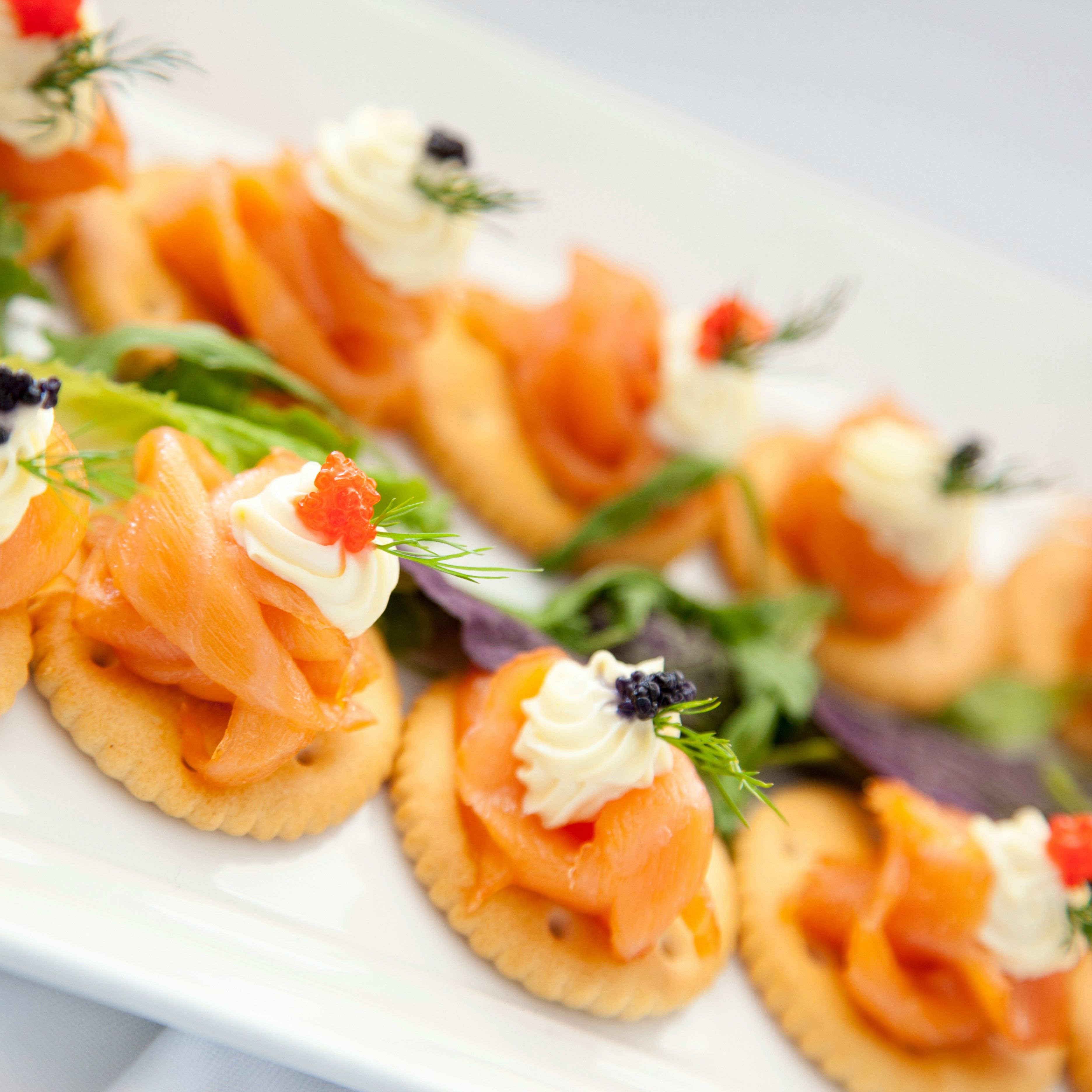 Close-up of smoked salmon canapés on crackers topped with cream cheese and garnish