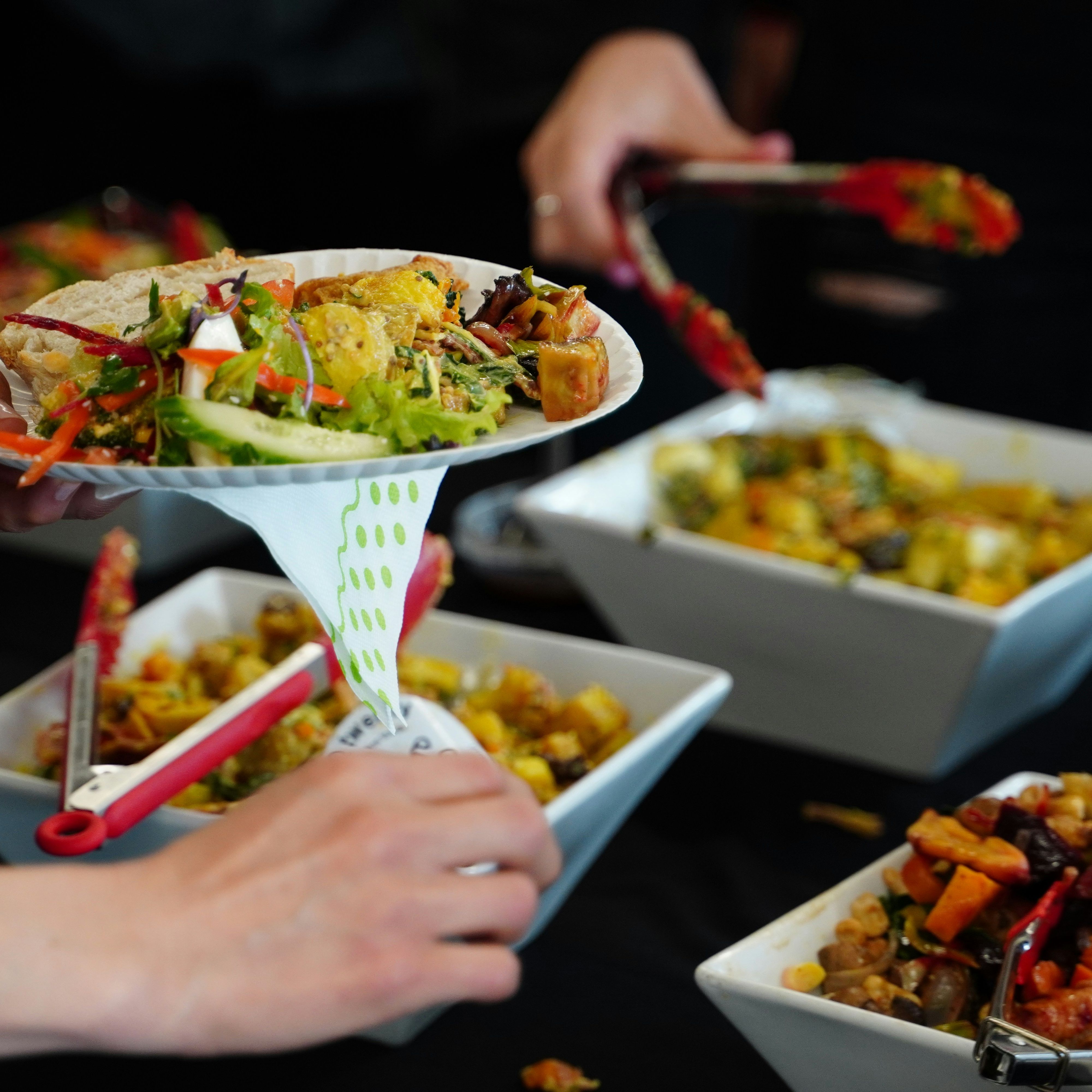 Person serving food onto a plate from a buffet with various salads and vegetables in white bowls.
