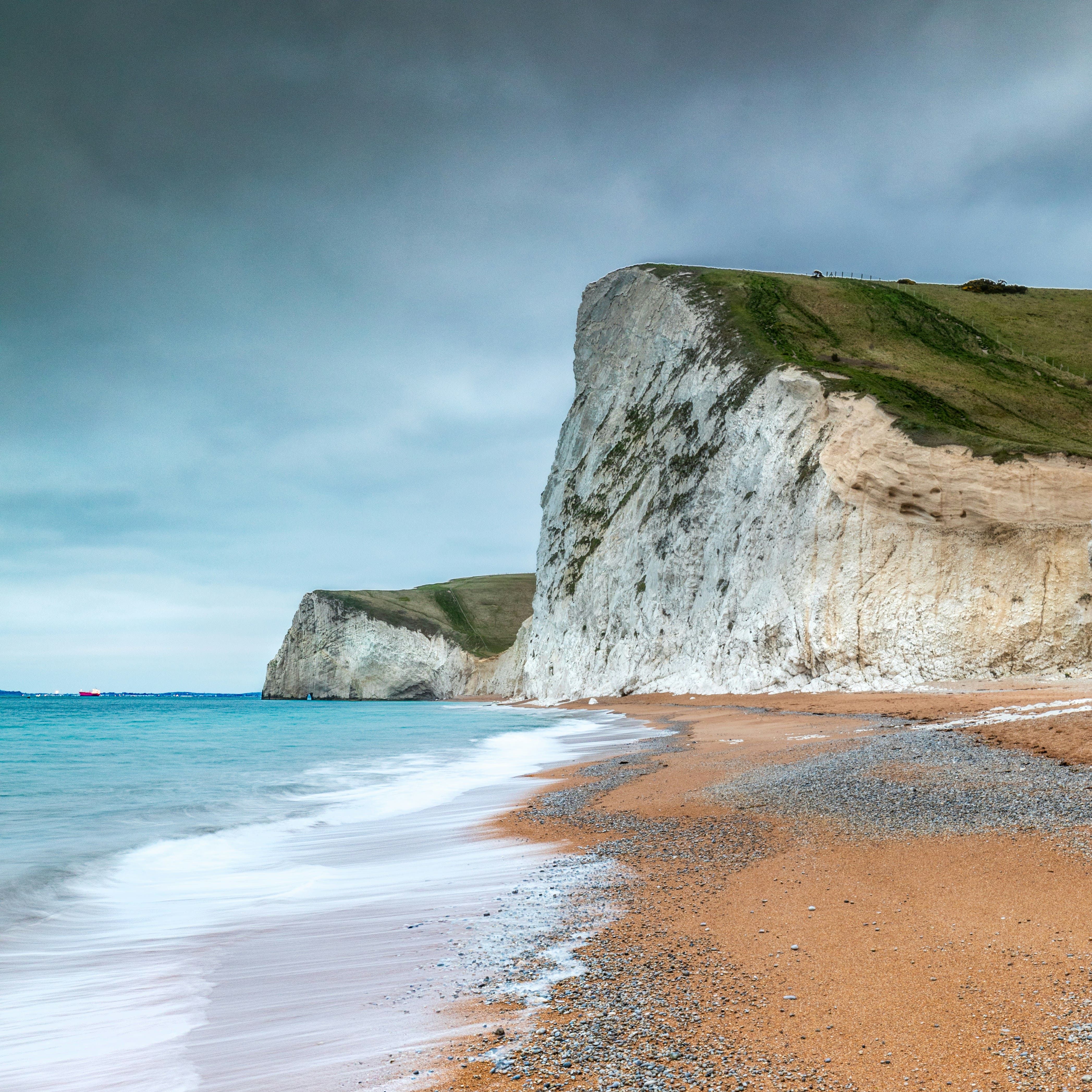 Steep white chalk cliffs beside a pebbled beach and turquoise sea under a cloudy sky