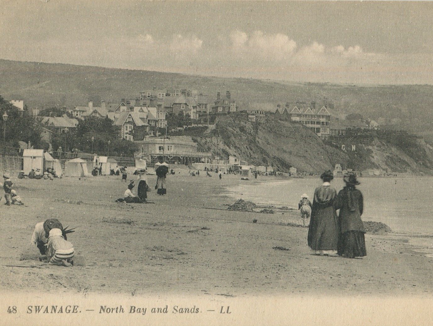 Vintage photograph of Swanage North Bay and Sands, showing people on the beach with cliffs and seaside buildings in the background.