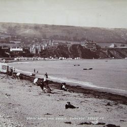 Vintage photograph of a beach scene with people relaxing on the sand and a grand hotel in the background, identified as Grand Hotel and Sands, Swanage.