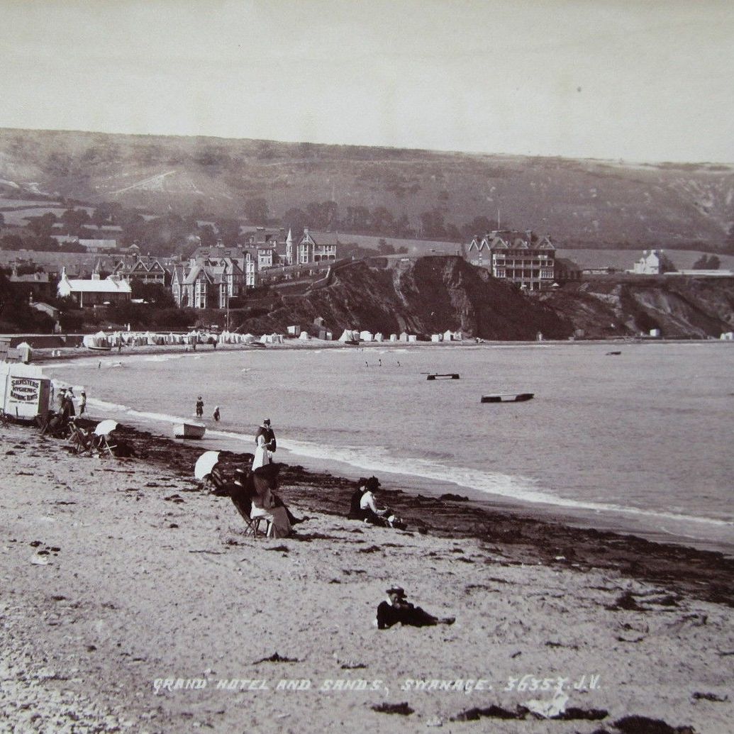 Vintage photograph of a beach scene with people relaxing on the sand and a grand hotel in the background, identified as Grand Hotel and Sands, Swanage.