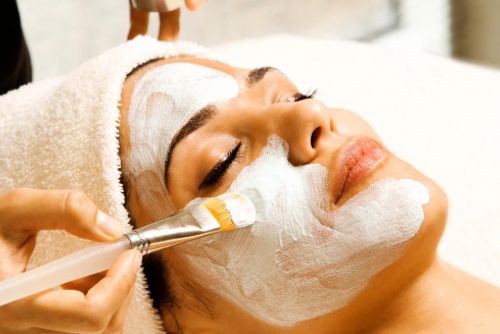 Woman receiving a facial treatment with a brush applying a white mask