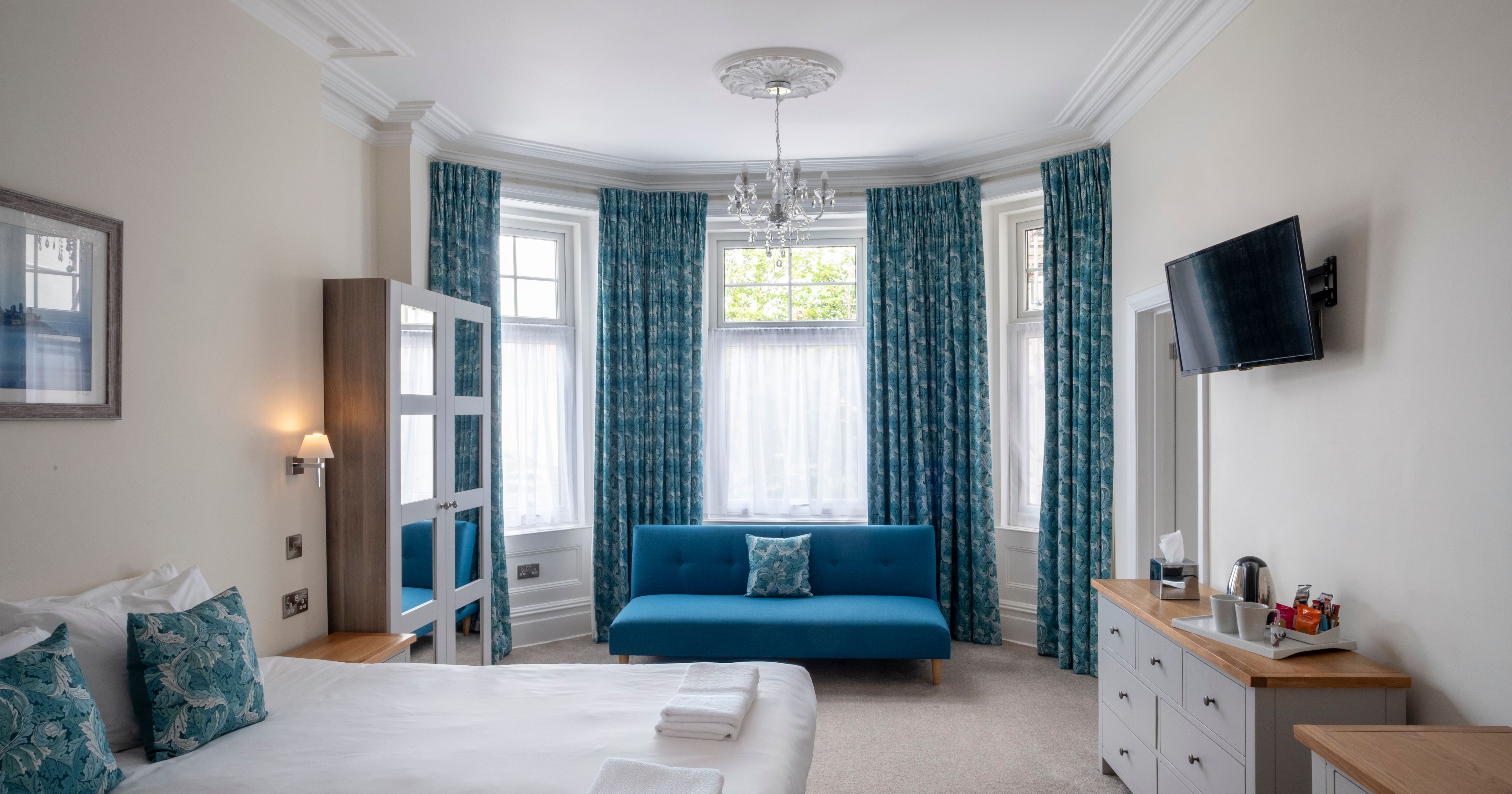 Bright bedroom with blue curtains, a blue sofa, large bed and modern furnishings
