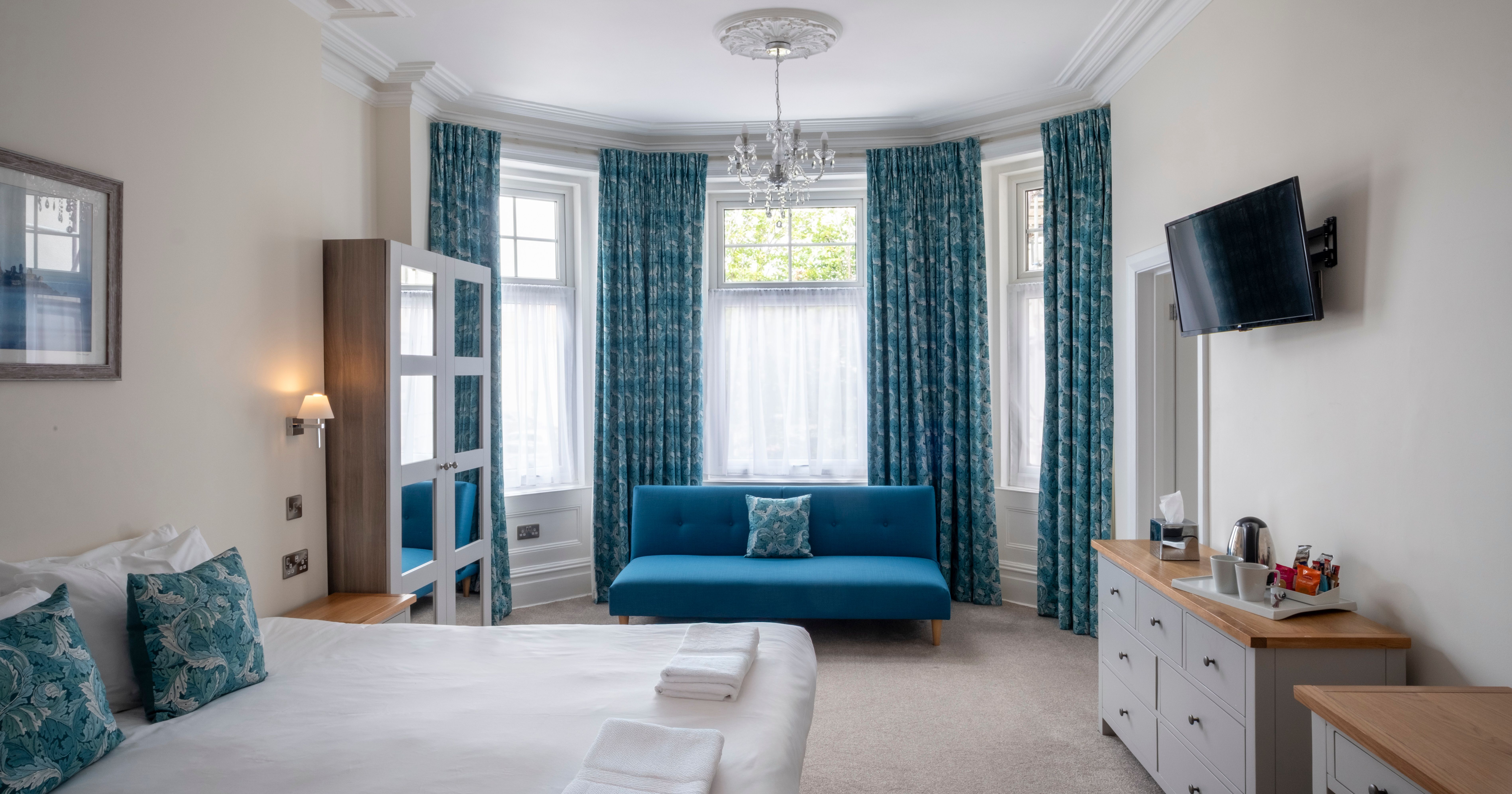 Bright bedroom with blue curtains, a blue sofa, large bed and modern furnishings