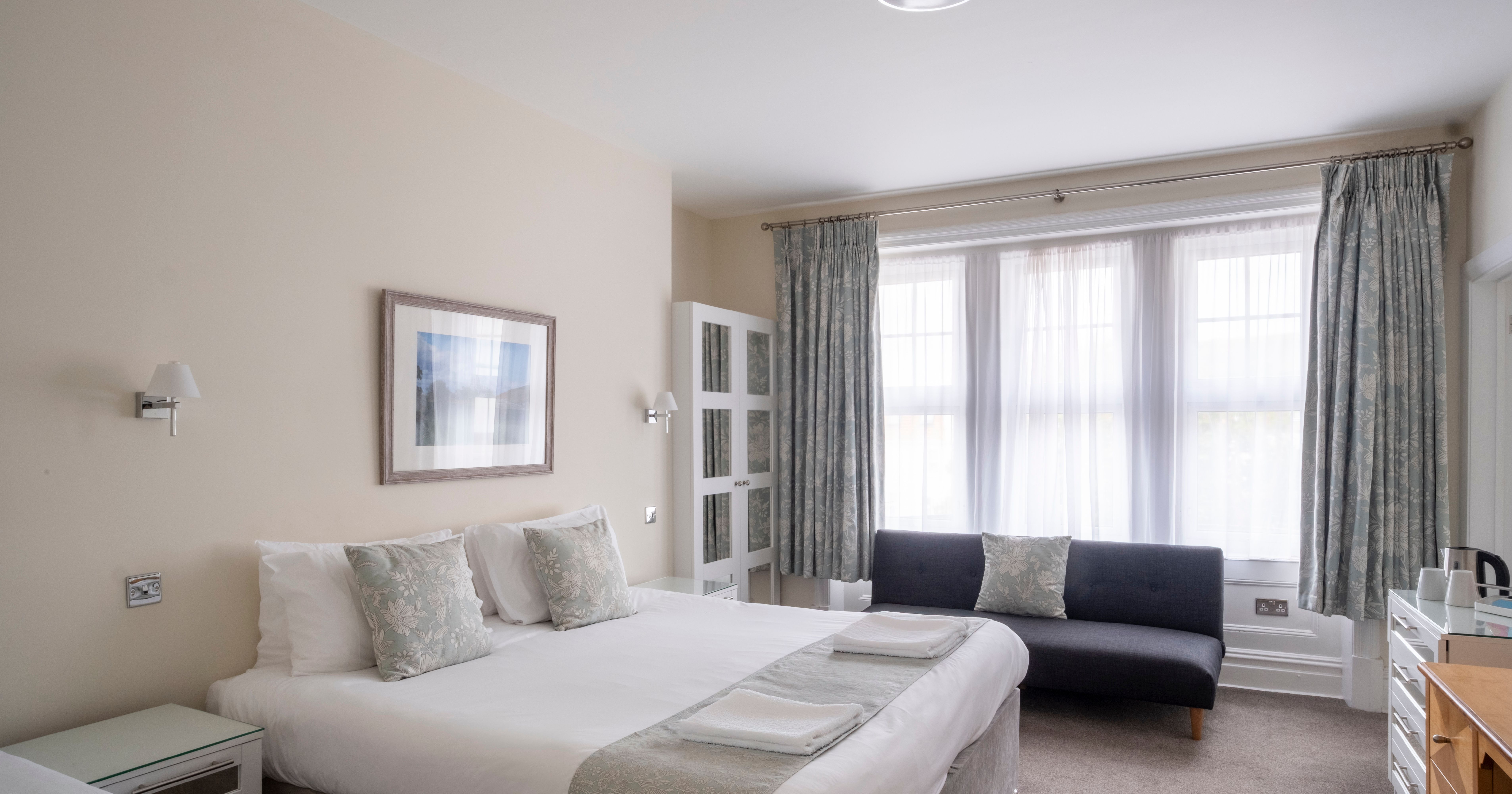 Bright and tidy hotel room with large bed, sitting area, and windows with curtains