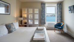 Hotel room with a large bed, mirrored wardrobe, blue floral curtains, and a window with a sea view.